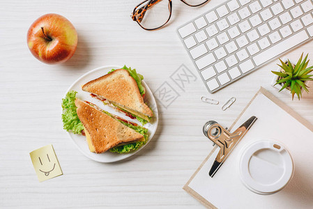 以三明治纸咖啡杯苹果和办公室桌边微笑符号为单位的工作图片