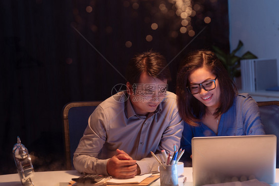 微笑的女商人在笔记本电脑上向男同事图片