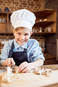 戴厨师帽的小男孩为披萨配料切蘑菇图片