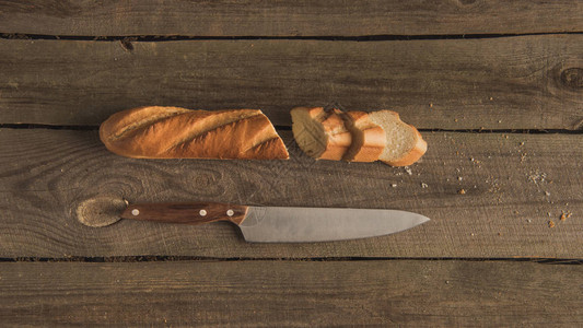 木桌上切片新鲜法式面包和刀的顶部视图图片