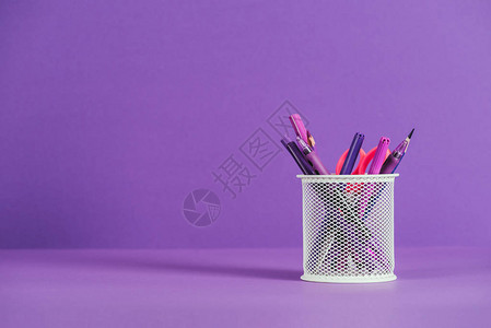 紫色表面上有各种钢笔和铅笔的筒图片