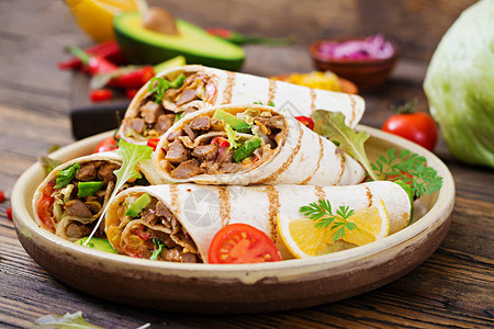 墨西哥卷饼包裹着木制背景上的牛肉和蔬菜背景图片