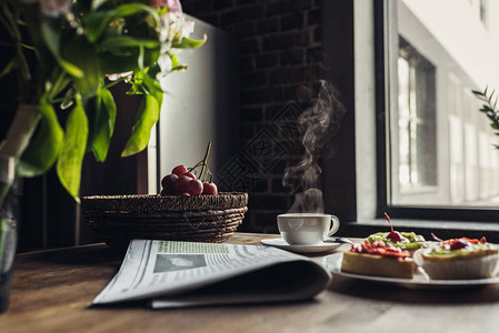 报纸早餐蛋糕和热咖啡在窗前的厨房桌图片