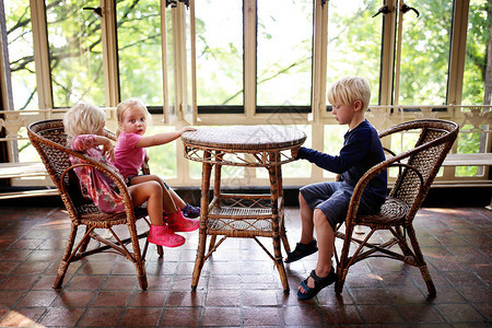 三个小孩坐在一个太阳室院子的老餐桌旁图片