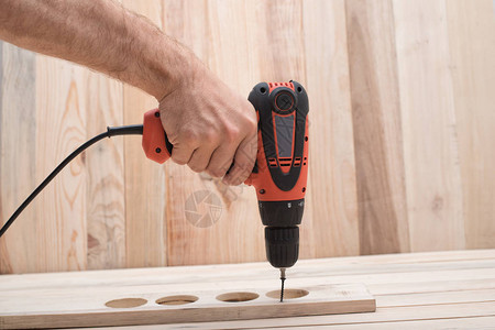男手中的电钻螺丝刀拧紧螺钉浅棕色木图片素材