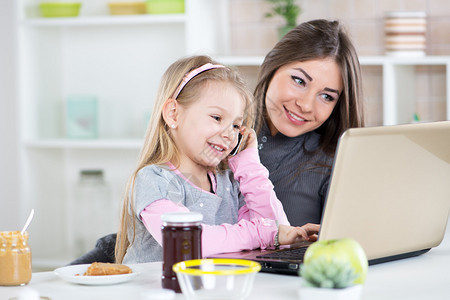妈和女儿早上在早餐时玩得开心可爱的小姑娘模仿妈用笔记本电脑图片