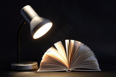 在深色背景上在发光的台灯附近打开书本图片