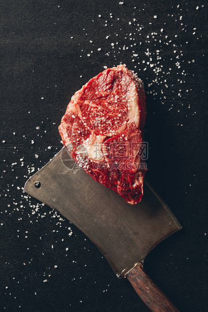 厨房桌面上生肉牛排盐和切肉刀的顶部视图图片