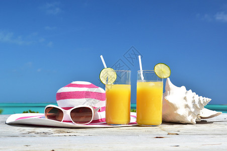 热带海滩的橙汁帽子太阳镜和海螺巴哈图片