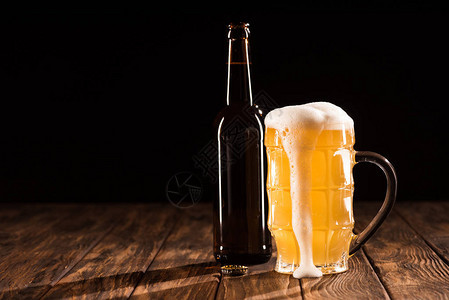 含泡沫的玻璃啤酒和在木制桌边的啤酒瓶图片