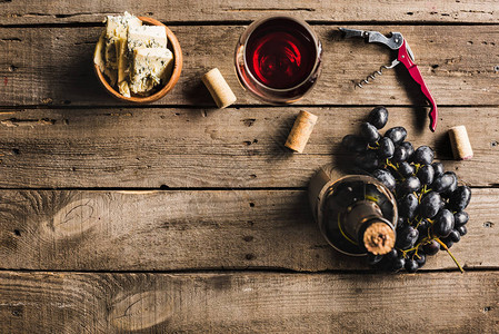 一瓶粉红葡萄酒开瓶器酒杯碗里的奶酪和木桌上的葡萄的顶视图图片