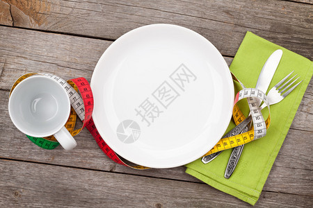 盘子有卷尺杯子刀子和叉子木桌上的减肥食品图片