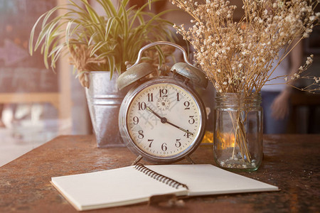 复古时钟和白花放在生锈的桌子上的笔记图片