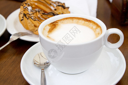 在木桌上的一杯咖啡背景是蛋糕图片