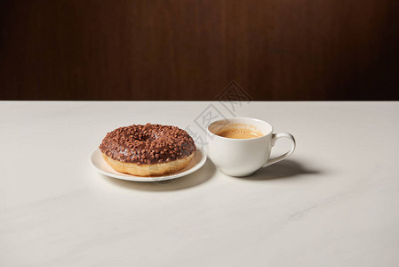 白桌上咖啡杯附近的釉面甜圈图片