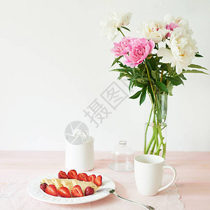 桌边的煎饼加草莓和咖啡在花瓶旁边图片