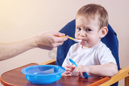 可爱的小男孩坐在厨房的椅子上吃着张大嘴巴妈手里图片