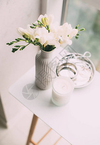 窗边桌上的花瓶和芳香蜡烛中的白色自由白布束图片
