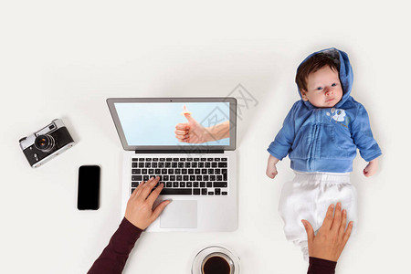 母亲在笔记本电脑上工作时抱着婴儿事业和家庭的平衡笔记本咖啡婴儿和女手从上图片
