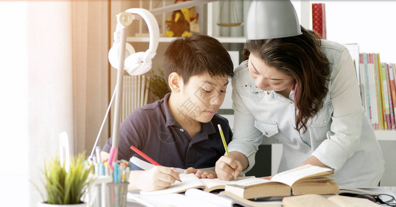 可爱的亚洲母亲帮助你的儿子在家里做功课用微图片