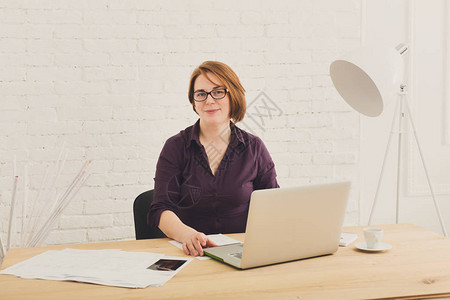 办公室里的中年妇女使用笔记本电脑和智能手机的女建筑师办公室工作人员戴防护眼镜的红发白种人妇女与计算机高调背景图片