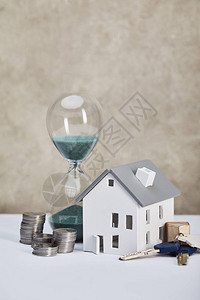 白桌上房屋模型带有沙玻璃银硬币和钥匙图片