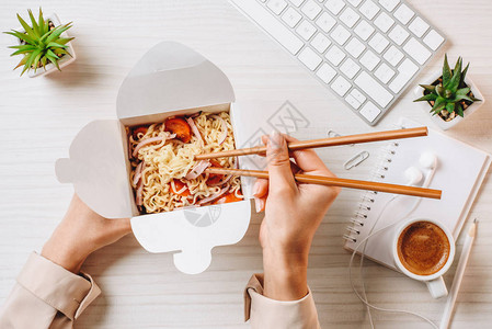 商业女商人在餐桌上用筷子和咖啡杯以及办公室电脑键盘吃图片
