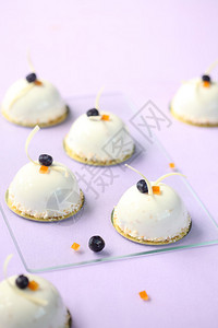 蓝莓和橙色的MousseCakes装饰着白色巧克力卷和烤椰子片图片