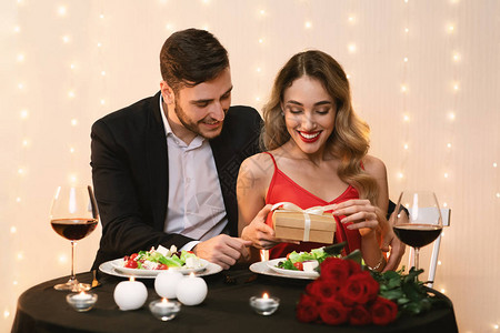 快乐的女人在餐厅约会时从男友那里拆开浪漫礼物背景图片