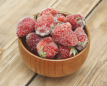 木制背景中木碗中的冷冻草莓图片