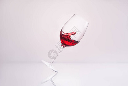 倾斜红酒杯在反射表面和白色上洒图片