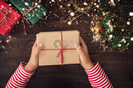 一个女人手拿着红丝带和雪在一张木桌上的圣诞礼物手工制作的圣图片
