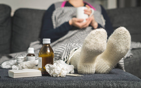 感冒药和生病的女人喝热饮料以从流感发烧和中康复桌子上的脏纸巾和纸巾穿着温暖的图片