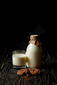 玻璃牛奶用纸包装的奶瓶和黑底巧克力饼干图片