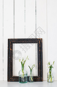 老式玻璃瓶中的白春花雪莲和白色谷仓墙背景图片
