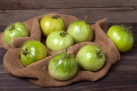未成熟的番茄用粗麻布的木制背景图片