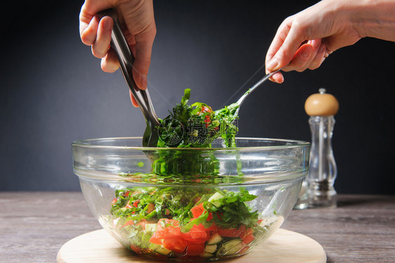 烹饪沙拉在家烹调蔬菜沙拉的少妇手用新鲜的西红柿搅拌素食沙拉图片