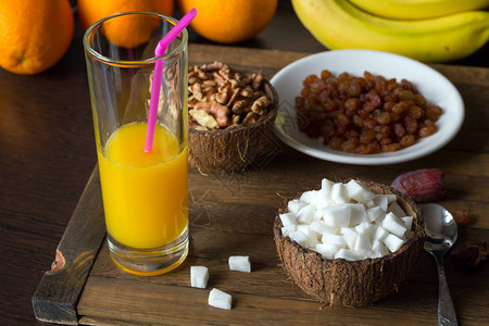 在木桌上的美味生食早餐椰子壳中的椰子肉和核桃仁在碗中一杯鲜榨橙汁盘子里的葡萄干橙子图片