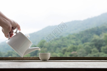 女人手拿着茶壶把白茶倒进绿色自然山底的杯子里图片