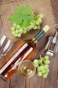 木桌背景上的一串葡萄白葡萄酒和开瓶器图片