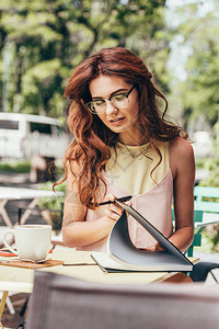 年轻女商人在眼镜中的肖像笔记本放在咖图片