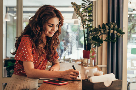 年轻博客用笔记在咖啡店加一杯咖啡的图片