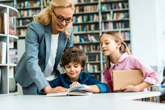 带着眼镜的快乐老师站在可爱孩子旁边在图书图片
