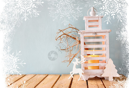 白色木制复古与燃烧的蜡烛木鹿圣诞礼物和木桌上的树枝带有雪花覆盖的图片