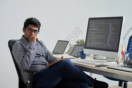 戴眼镜的印度程序员坐在工作场所前的椅子上思考工图片