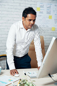 印度中年成商人站在办公桌台和计算机工作上图片