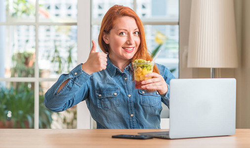 红发女人在家用电脑笔记本电脑吃水果背景图片
