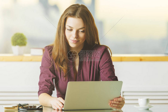 利用膝上型电脑在现代城市办公室的玻璃桌面上安装有吸引力的女士肖像图片