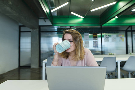 一名疲劳的办公室工人在电脑上工作时喝咖啡图片