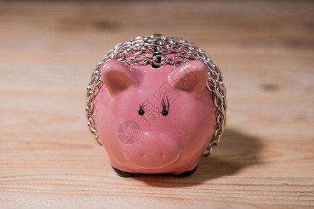近视粉色陶瓷小猪银行在木桌顶链条上的铁链中背景图片